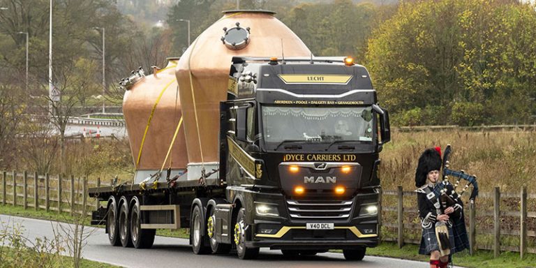 Piper walking ahead of a lorry carrying two massive copper vessels